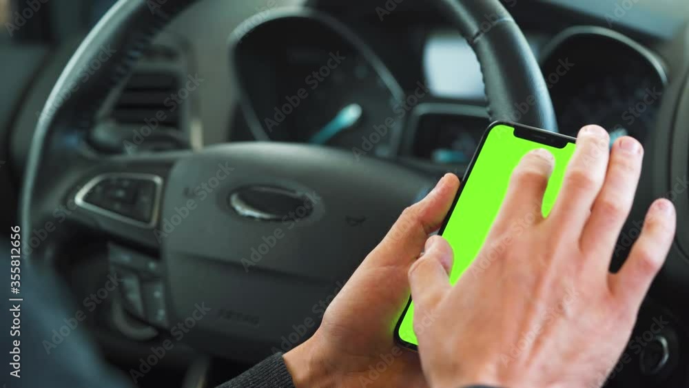Driver using a smartphone inside the car. Chromakey smartphone with green screen. Auto navigation. Internet addiction Driver using a smartphone inside the car. Chromakey smartphone with green screen. Auto navigation. Internet addiction