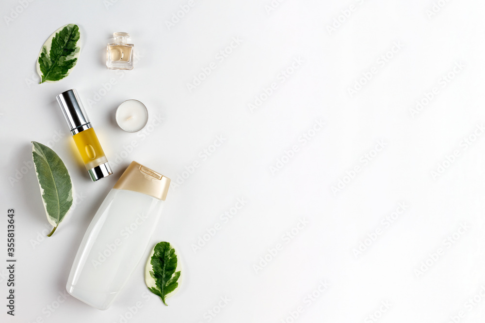 Cosmetics and self-care. Green leaves, shower gel, perfume, oil in a tube and a candle are laid out on a white background. Flat lay. Copy space Cosmetics and self-care. Green leaves, shower gel, perfume, oil in a tube and a candle are laid out on a white background. Flat lay. Copy space
