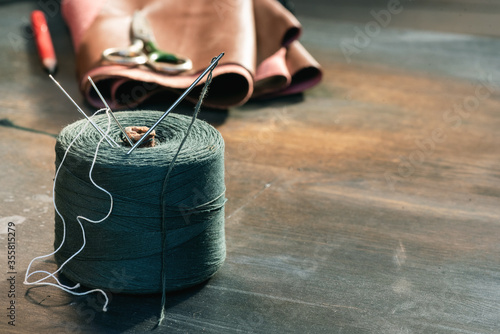 Tableau sur toile Sewing thread spool with needle, leather and scissors on the table close up