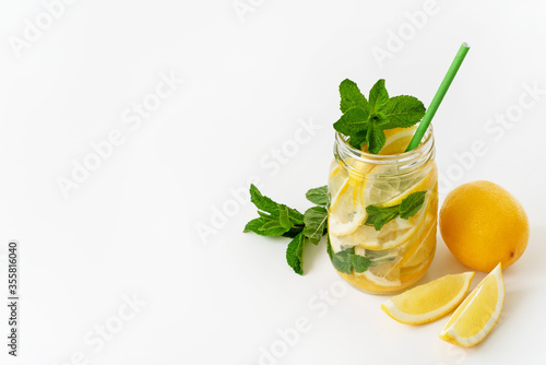 Fresh lemonade in a mason jar with eco-friendly straw, lemons and mint on the white background. Refreshing summer drink. Copy space.