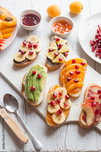 Sweet toast with jam and various fruits apricots, peaches, bananas, oranges and avocado decorated with pomegranates on top.