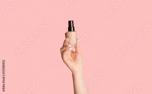 Obraz na plátně Cropped view of millennial girl showing bottle of makeup foundation on pink back