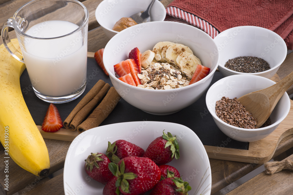 Healthy breakfast with bowl of oatmeal, flaxseed, chia seeds, strawberries,banana, cinnamon sticks and peanut butter on wooden table Healthy breakfast with bowl of oatmeal, flaxseed, chia seeds, strawberries,banana, cinnamon sticks and peanut butter on wooden table