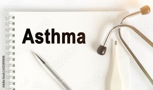 On the table are a stethoscope  a thermometer  a pen and a notebook with the inscription -Asthma