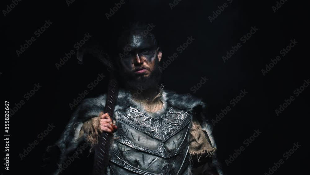 An aggressive Viking in wool armor puts an axe on his shoulder and glares at the camera. A Viking in armor on a black background with a two handed axe looks at the camera An aggressive Viking in wool armor puts an axe on his shoulder and glares at the camera. A Viking in armor on a black background with a two handed axe looks at the camera