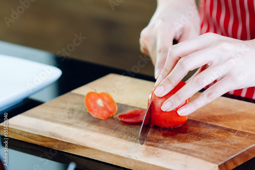Asian female chef dressed in an apron cooking in the kitchen making salad cutting tomatoes
