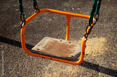 An empty old orange swing on a Playground on a summer evening.