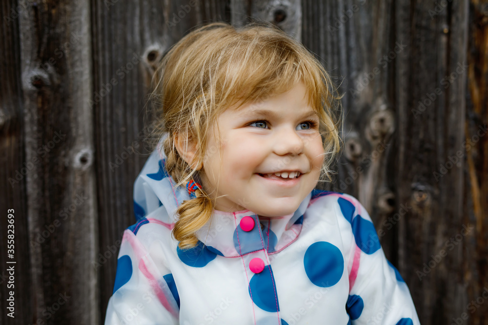Outdoor portrait of happy smiling little toddler girl wearing rain jacket on rainy cloudy day. Cute healthy child in colorful clothes outdoor activity Outdoor portrait of happy smiling little toddler girl wearing rain jacket on rainy cloudy day. Cute healthy child in colorful clothes outdoor activity