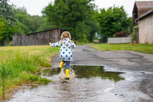 Konstfotografi Little toddler girl wearing yellow rain boots, running and walking during sleet on rainy cloudy day