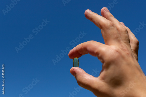A man s hand holds a yellow capsule against a blue sky