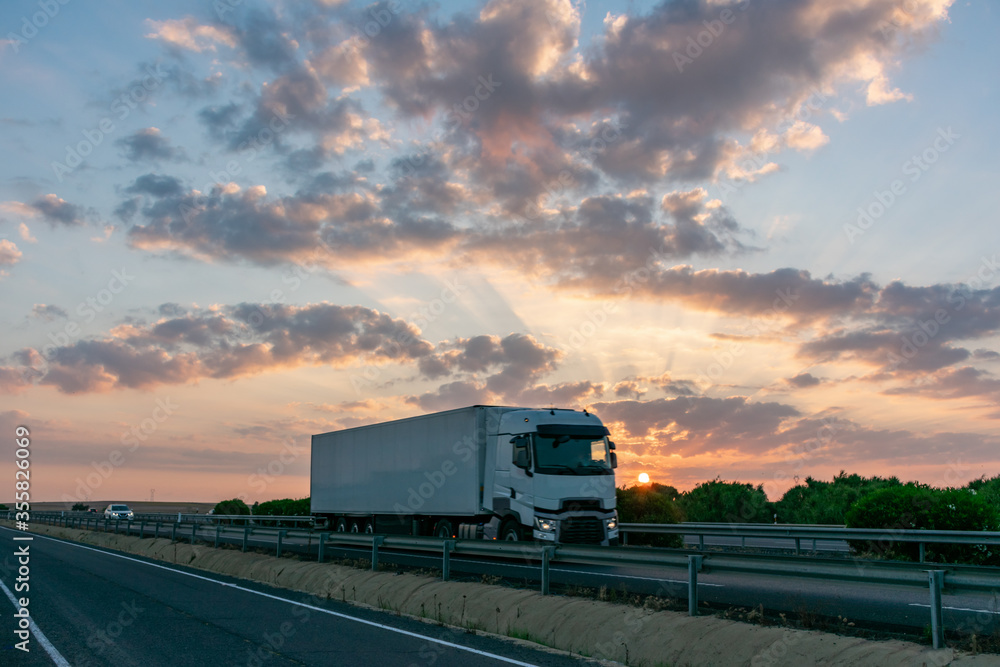 Refrigerated truck driving on the highway with reflections of the sunset sun in the sky with clouds