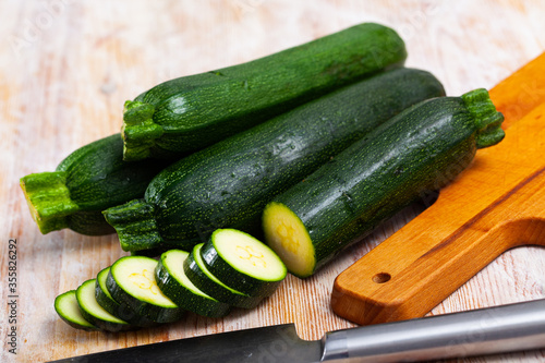 Closeup of fresh zucchini with chopped slices on wooden surface