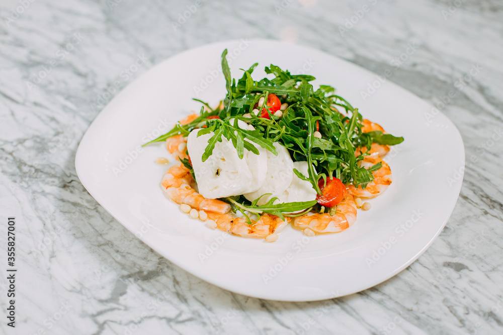 salad with shrimp, cheese and arugula in a white plate on a marble table