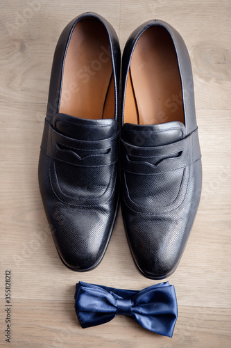 black stylish leather shoes and a blue butterfly on a wooden floor. groom's morning. gentleman's accessories.
