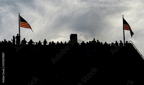 Silhouette of people standing on top of a stadium with .Two United States of America flags flying on both sides .