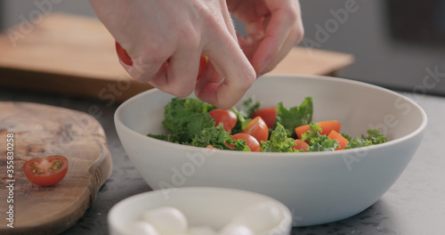 man add tomato into salad with kale and in white bowl on kitchen countertop