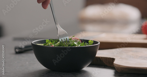 man tries fresh salad with radish, cucumber and herbs in black bowl