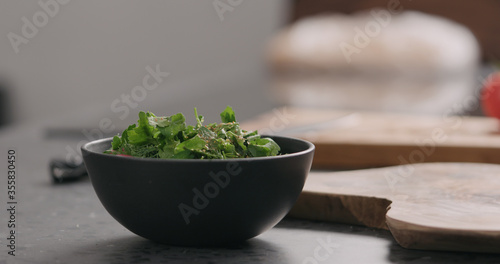 seasoning fresh salad with radish, cucumber and herbs in black bowl