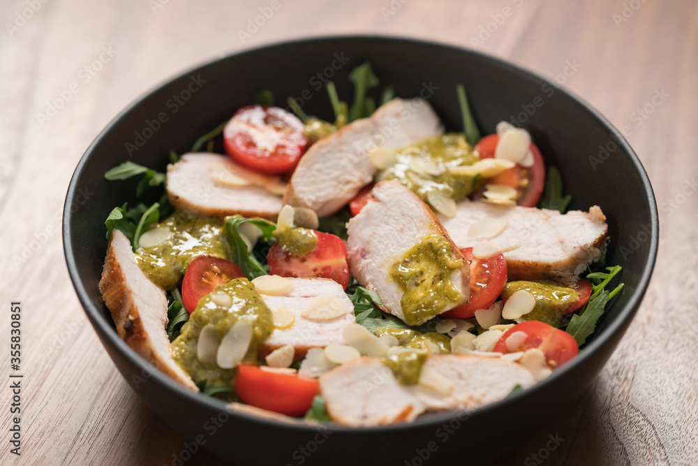 Salad with chicken, tomatoes and arugula in black bowl on walnut wood background Salad with chicken, tomatoes and arugula in black bowl on walnut wood background