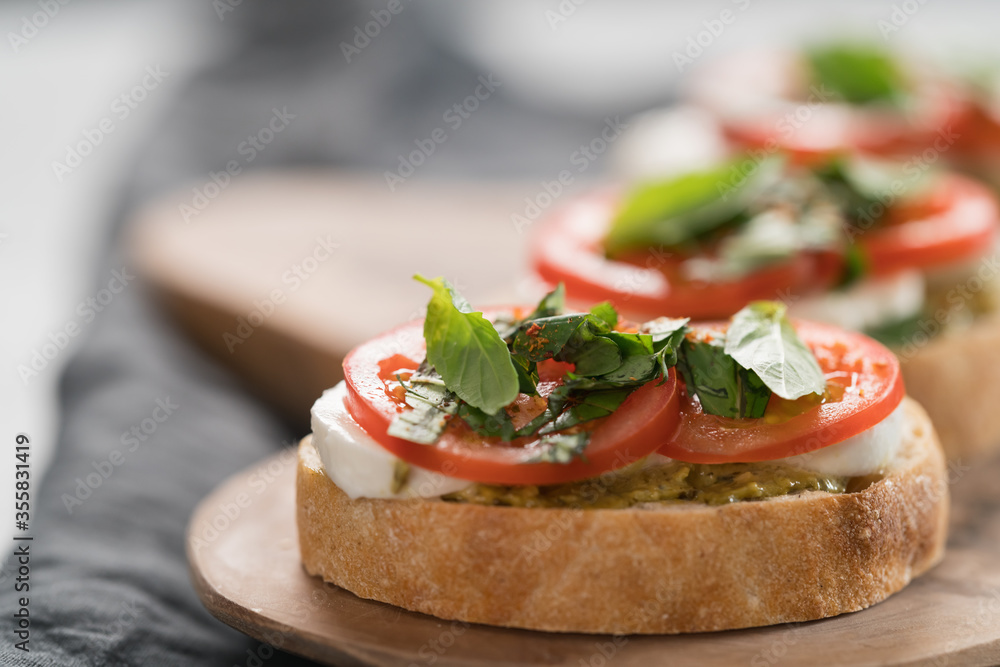 Bruschetta with mozzarella, tomatoes and basil with pesto on olive wood board Bruschetta with mozzarella, tomatoes and basil with pesto on olive wood board