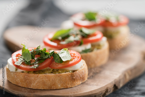 Bruschetta with mozzarella, tomatoes and basil with pesto on olive wood board