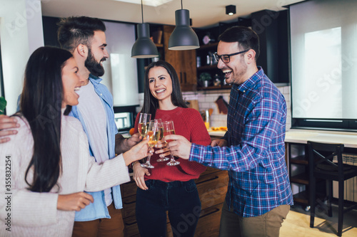 Young people cheering with champagne flutes and looking happy while having home party.