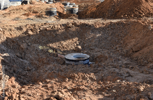 Laying concrete manholes and heating drain pipes and for stormwater system in trench at construction site. Sewerage manhole and pipes line under construction.  Chambers and Pump Station