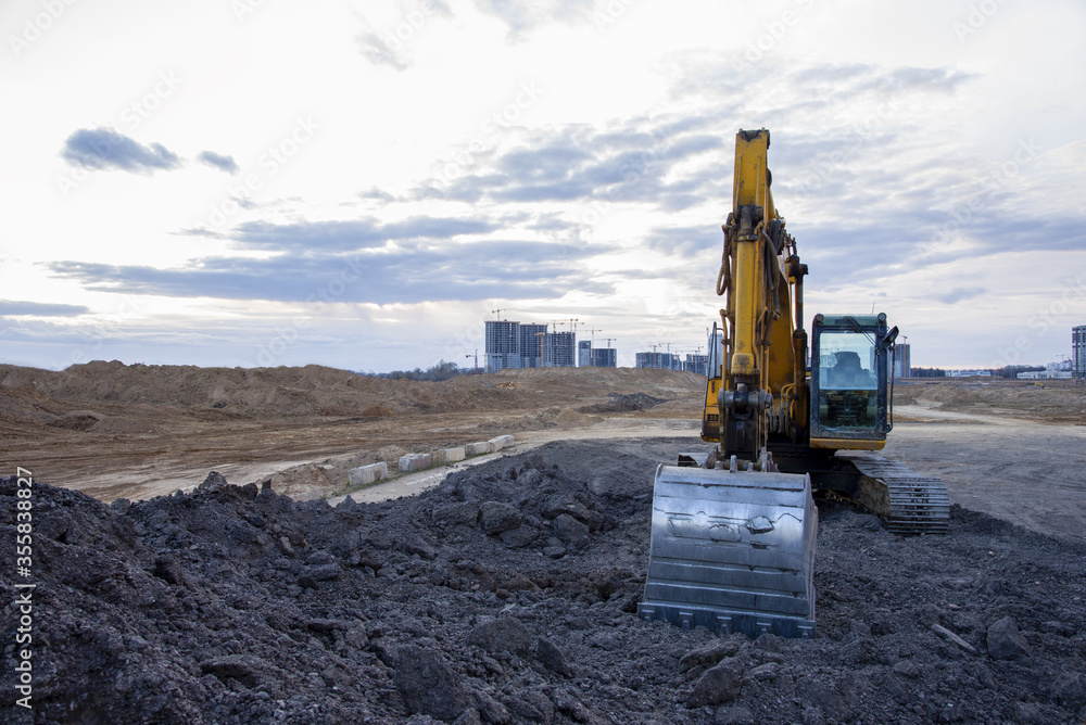 Excavator work at constrruction site on sunset background. Backhoe digs gravel and old concrete. Recycling old asphalt at a landfill for the disposal of construction waste. Construction machinery