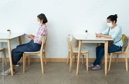 Asian woman wearing face mask and keep social distanicng by sitting on each table in the restaurant during covid-19 or coronavirus outbreak. new normal lifestyle concept
