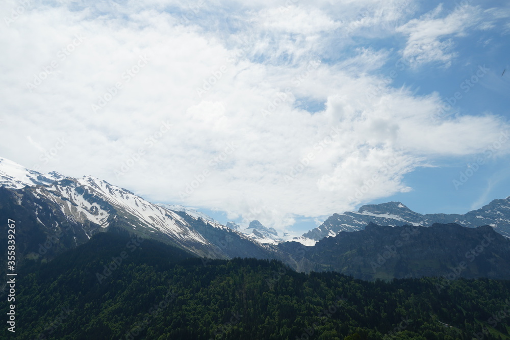 Rock alpine mountains in Engelberg, Obwalden canton in Switzerland. Lower altitude mointains with mixed forests in the foreground. The sky is covered with cirrus clouds.