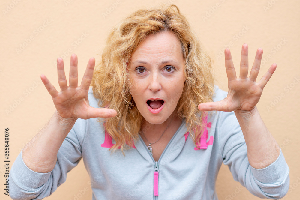 Obraz premium A white woman makes a funny expression by raising her hands close to her face