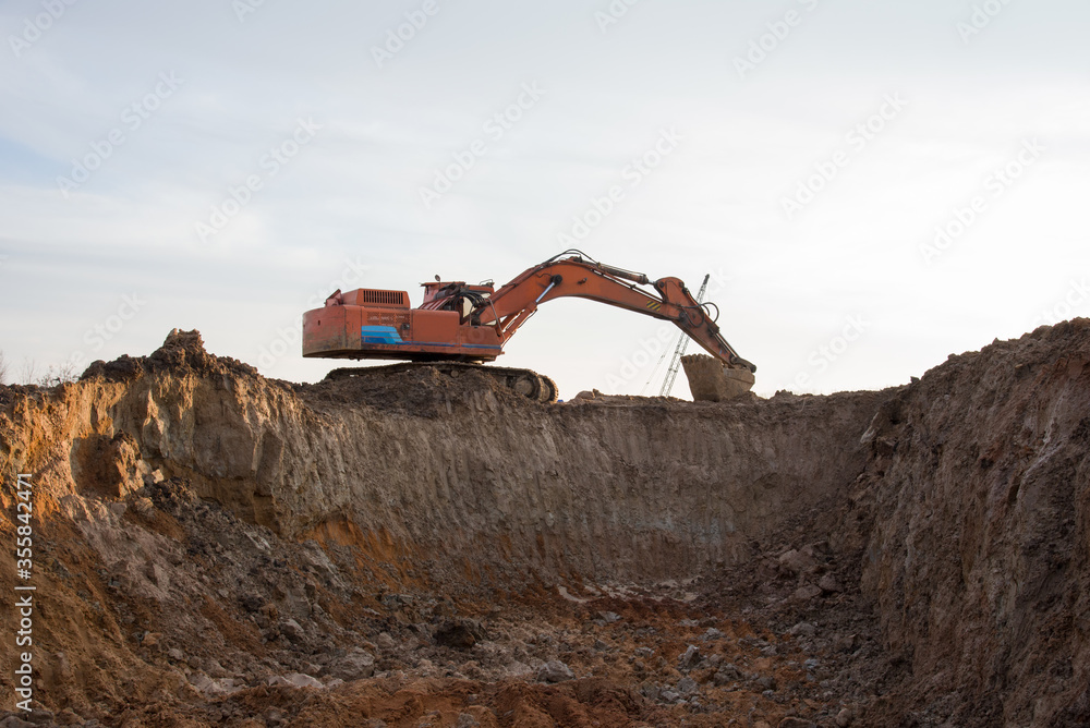 Large excavator working at construction site. Backhoe during earthworks on sand open-pit. Digging ground for the foundation and for laying sewer pipes district heating. Earth-moving heavy equipment