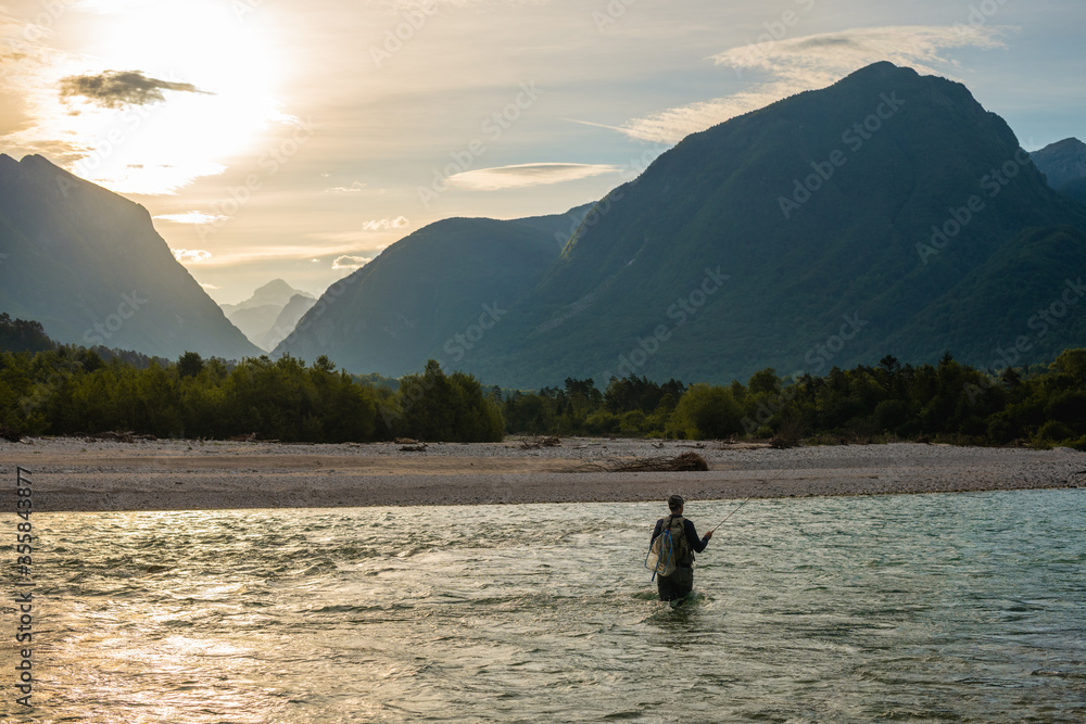 Silhouette of a fly fisherman casts his line while wading in the middle of a river Silhouette of a fly fisherman casts his line while wading in the middle of a river