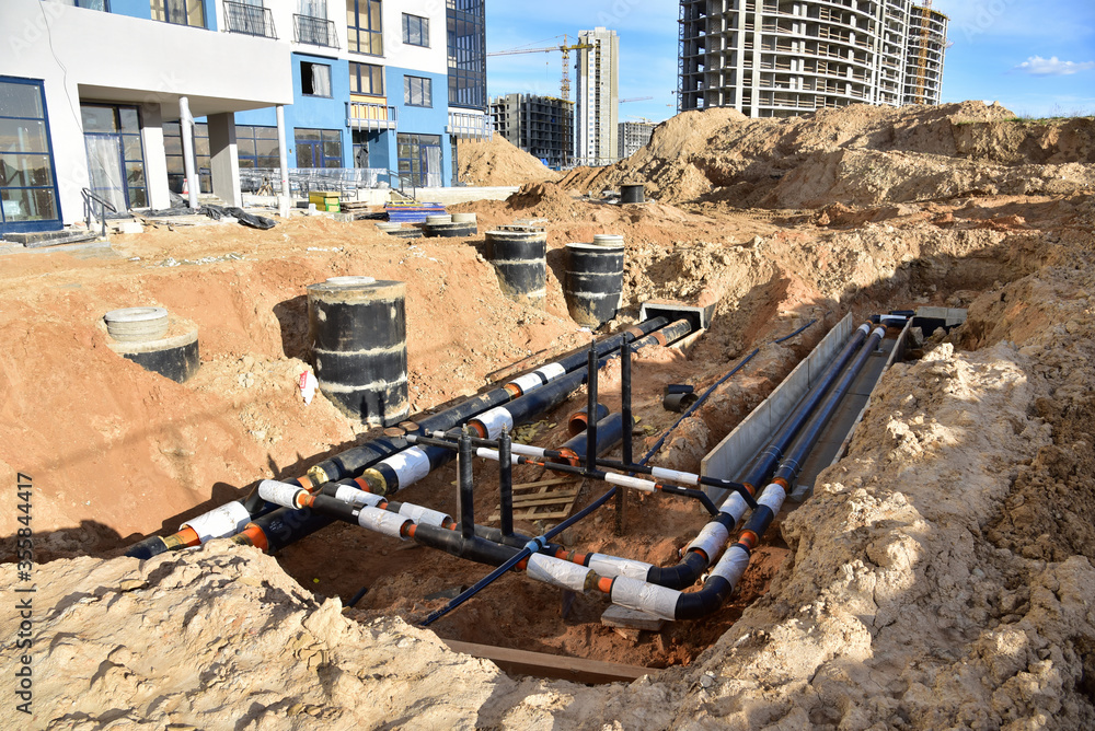 Laying heating pipes in trench at construction site. Installing concrete  sewer wells and underground storm systems of sanitary water main. Cold and hot  water heating system of the apartments in house Stock