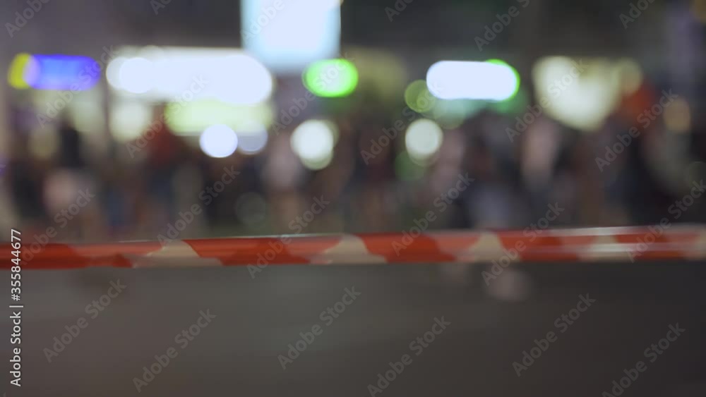 Police warning tape red & white in the city streets at night people in background Police warning tape red & white in the city streets at night people in background