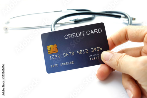 Woman 's hand holding credit card  stethoscope background.Health care costs concept.