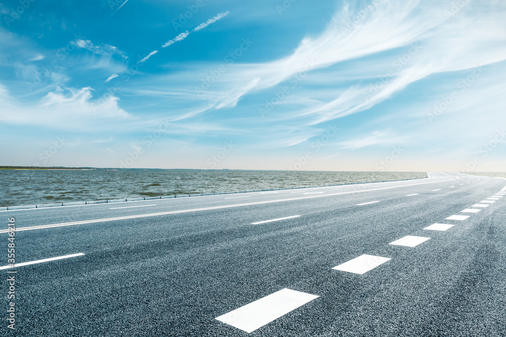 Fototapeta premium Asphalt road and lake water under blue sky.