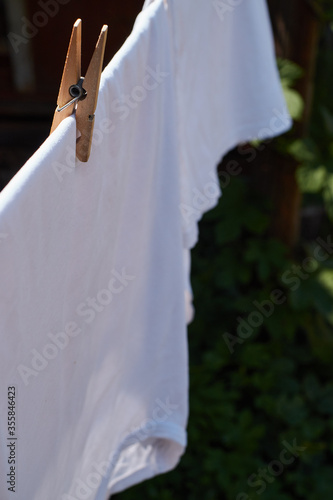 White linen is dried on a hanger. Clothes hanging on a clothesline are drying outside
