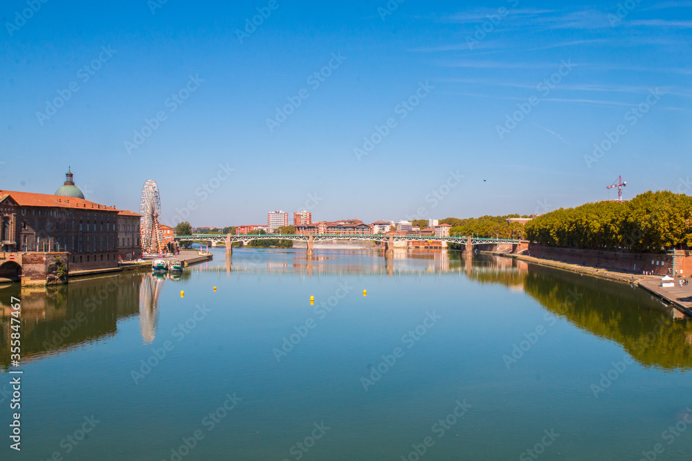 Toulouse landmarks on the bank of river Garone. Hospital de La Grave and Ferries Wheel reflected in Garone river.