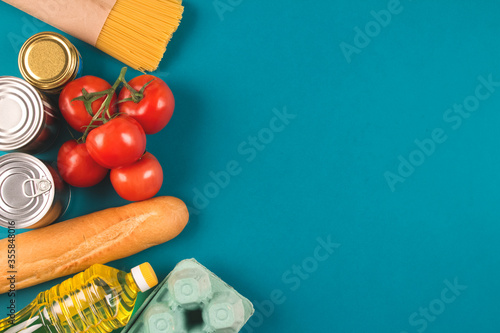 Food donations on green background with copyspace - pasta, fresh vegatables, canned food, baguette, eggs, organic oil. Donation or delivery food concept