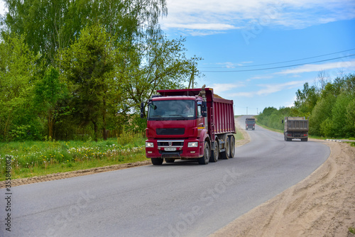Tipper Dump Truck transported sand from the quarry on driving along highway. Modern Heavy Duty Dump Truck with unloads goods by itself through hydraulic or mechanical lifting