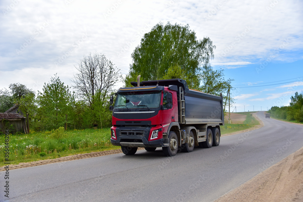 Tipper Dump Truck transported sand from the quarry on driving along highway. Modern Heavy Duty Dump Truck with unloads goods by itself through hydraulic or mechanical lifting Tipper Dump Truck transported sand from the quarry on driving along highway. Modern Heavy Duty Dump Truck with unloads goods by itself through hydraulic or mechanical lifting