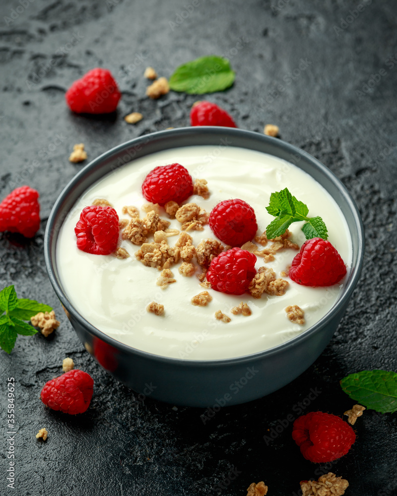 Greek yogurt with granola and raspberry in black bowl. Healthy breakfast food or snack Greek yogurt with granola and raspberry in black bowl. Healthy breakfast food or snack