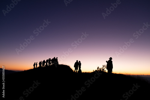 Silhouette of group people standing on the mountain and look to the forward at twilight time.