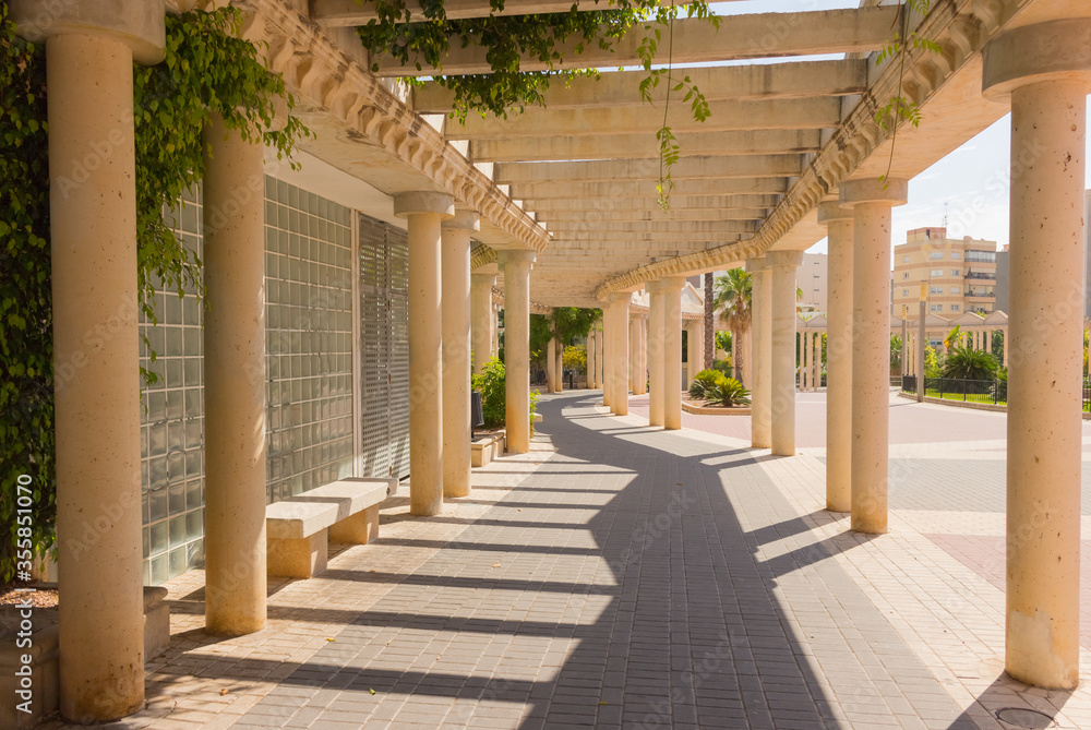 Long empty corridor with arch and stone columns in the park, old town, Calpe, Spain