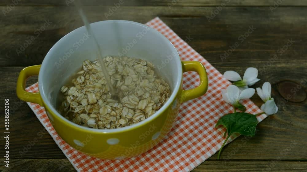 Vegetarian healthy breakfast with porridge. Oatmeal flakes in yellow bowl poured with water. On kitchen table. Close-up. Indoor. Vegetarian healthy breakfast with porridge. Oatmeal flakes in yellow bowl poured with water. On kitchen table. Close-up. Indoor.
