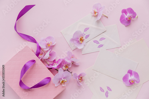 Pink gift bag and flying orchid flowers on light pink background. Top view greeting card with delicate flowers. © svittlana