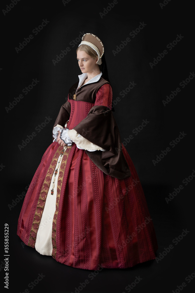 A young woman in a red Tudor dress against a black bacdrop A young woman in a red Tudor dress against a black bacdrop