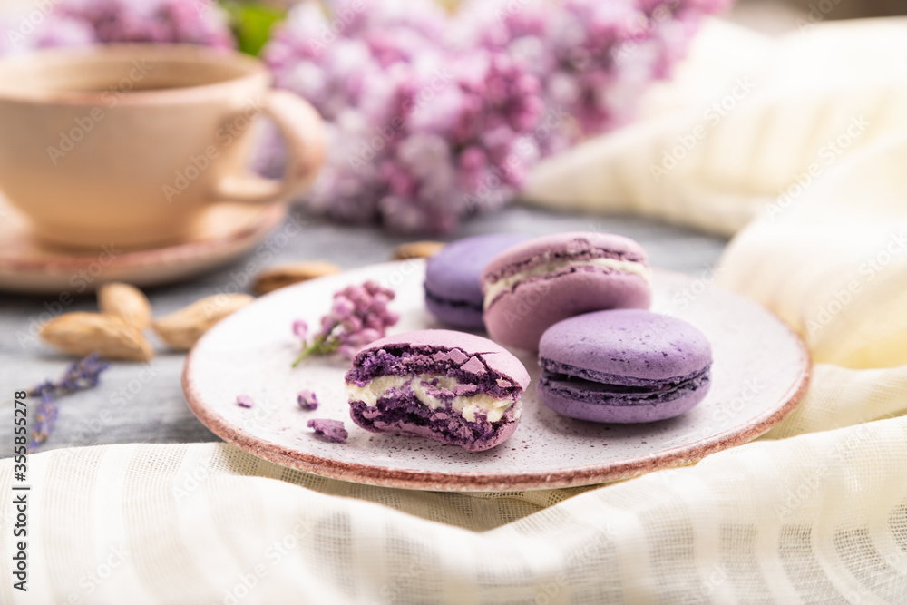 Purple macarons or macaroons cakes with cup of coffee on a gray wooden background. Side view, selective focus. Purple macarons or macaroons cakes with cup of coffee on a gray wooden background. Side view, selective focus.