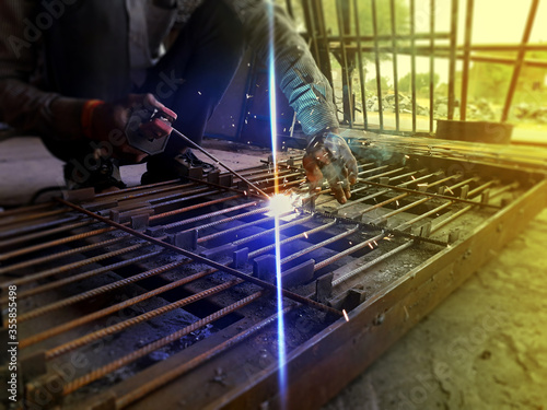 Generating blue sparks while worker welding on iron in industrial workshop